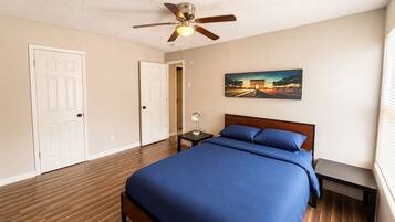 A bedroom with a bed, a ceiling fan, a nightstand, a lamp, and a painting on the wall.