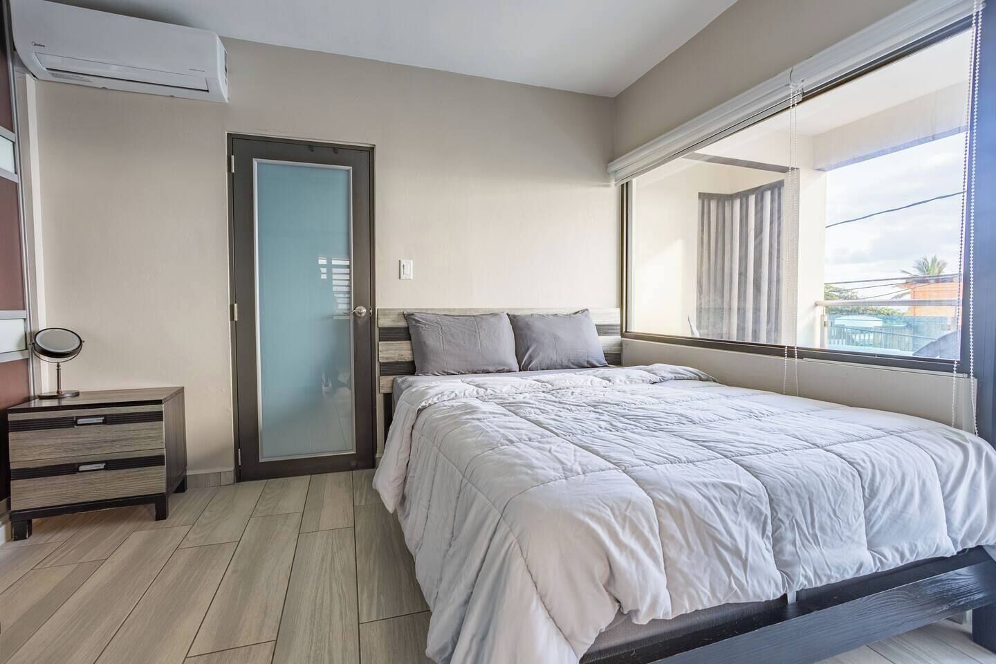 A bedroom with a bed, a dresser, a mirror, a sliding glass door, and a large window with a view.