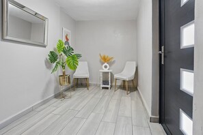 A hallway with a mirror, two white chairs, a potted plant, and a small table with a vase. - Arecibo 3BR | Beach Views | Jacuzzi (Arecibo)
