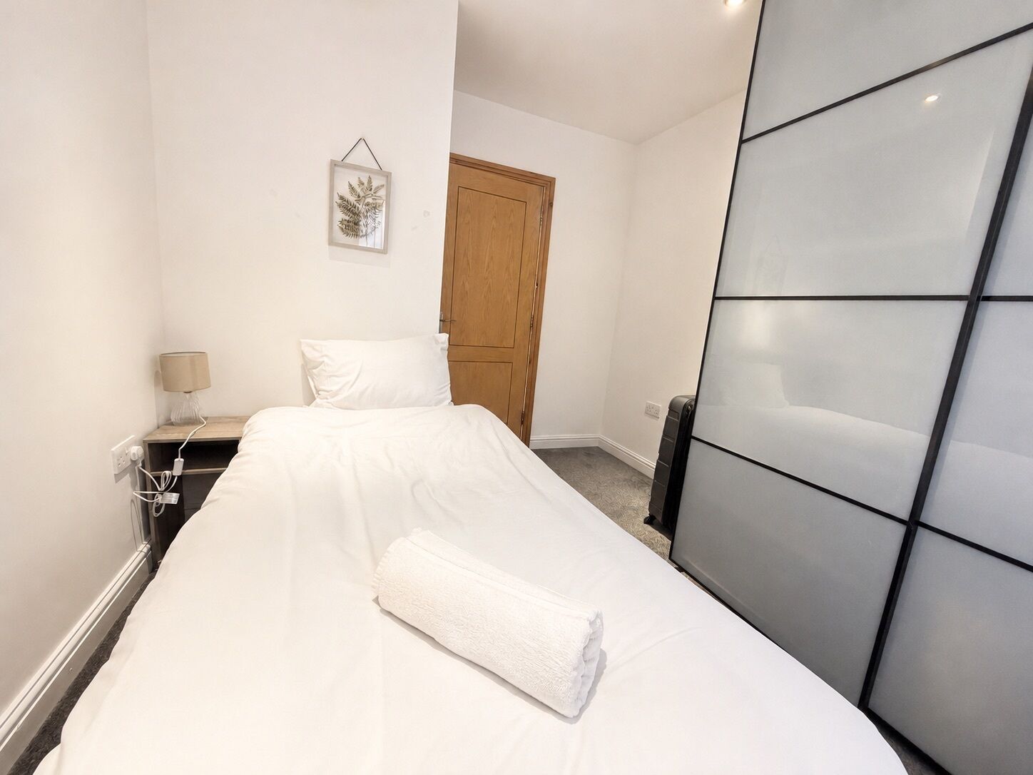 Une chambre d’hôtel avec un lit, une table de chevet, une lampe, une porte en bois et un tableau accroché au mur.