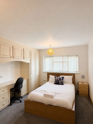 A bedroom with a bed, a desk, a chair, a nightstand, and a window with blinds. - Large 6 bedroom house in Oxford near John Radcliffe Hospital with parking for (Oxford)