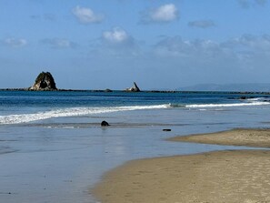 Ein Strand mit blauem Himmel, ruhigem Wasser und Felsen in der Ferne.