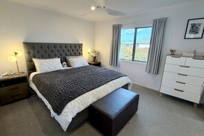 Un dormitori amb un llit gran, tauletes de nit, una petita còmoda i una finestra amb cortines.