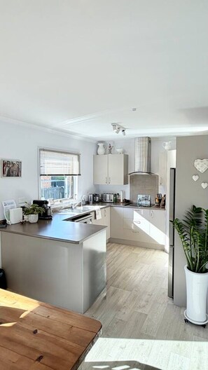 A modern kitchen with a central island, built-in appliances, and a view to the outside. - Mangawhai Village Hideaway (Mangawhai)
