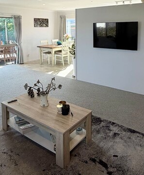 A living room with a wooden coffee table, a vase with flowers, and a flat-screen TV mounted on the wall. - Mangawhai Village Hideaway (Mangawhai)