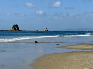 Una platja amb cels clars, aigua tranquil·la i roques.