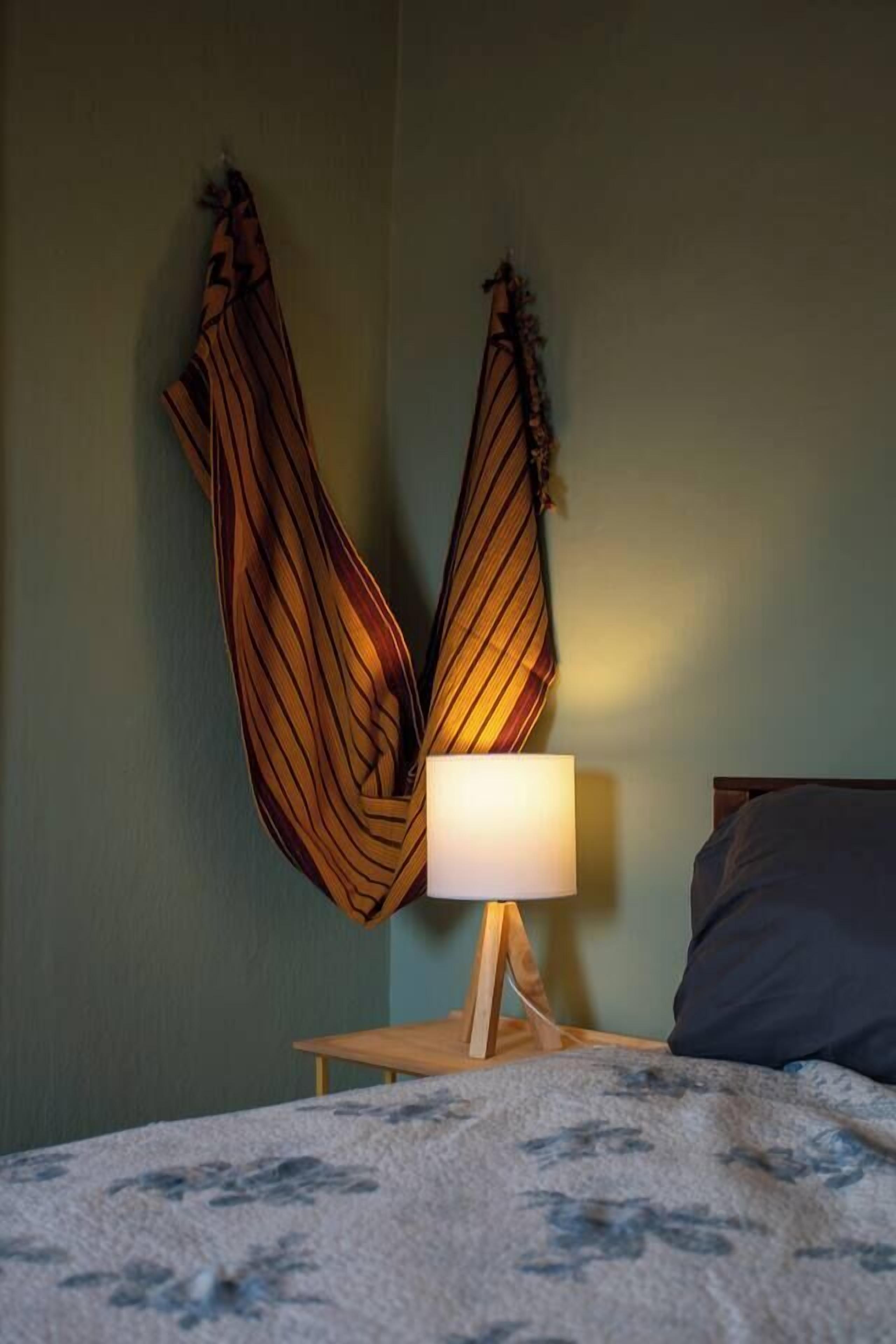 Una habitación con cama, mesita de noche, lámpara y un adorno en la pared.