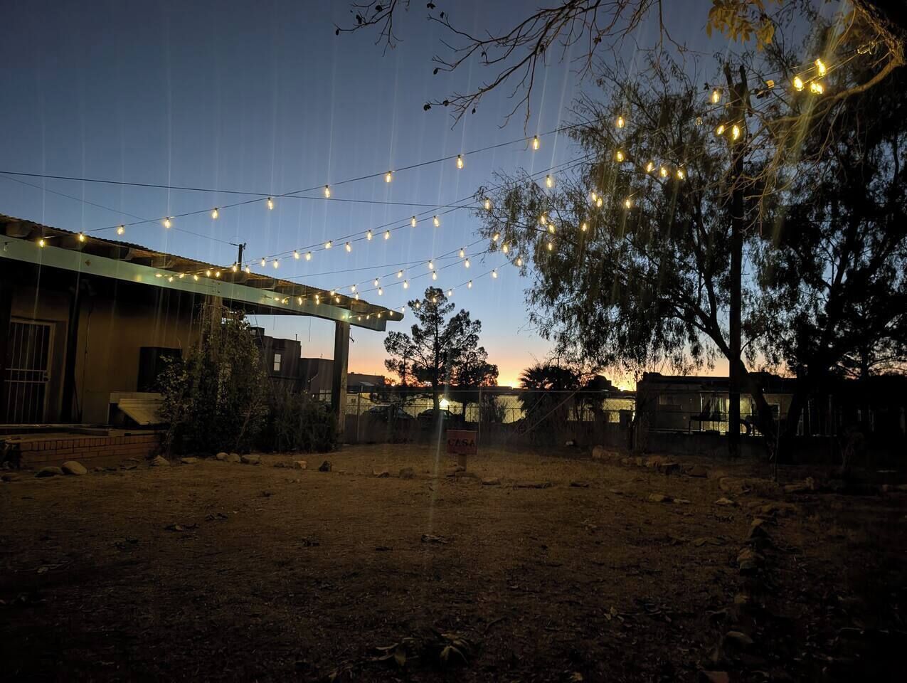 Un espace extérieur clos, agrémenté de guirlandes lumineuses, un bâtiment doté d’un toit plat et une enseigne sur laquelle on peut lire « CASA ».