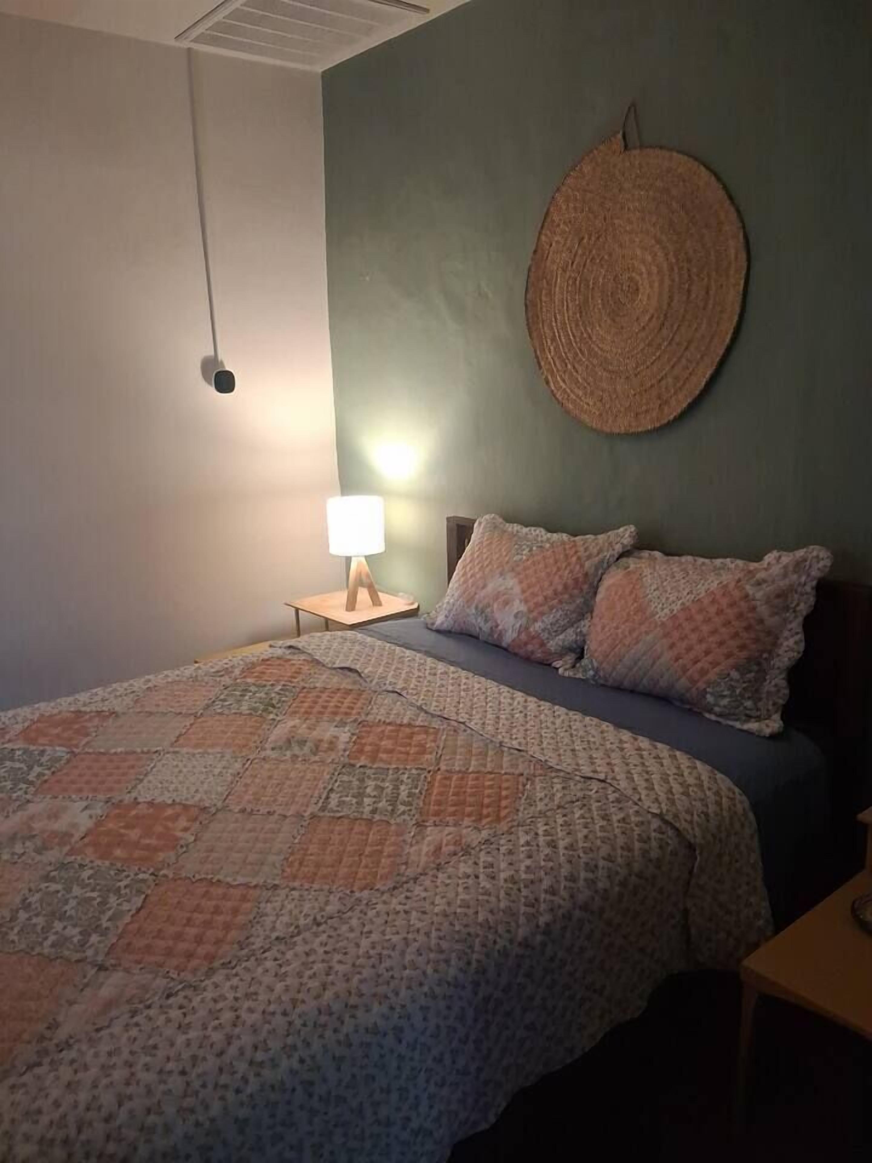 Une chambre à coucher comprenant un lit, une lampe de chevet, un objet circulaire fixé au mur et un luminaire fixé au mur.