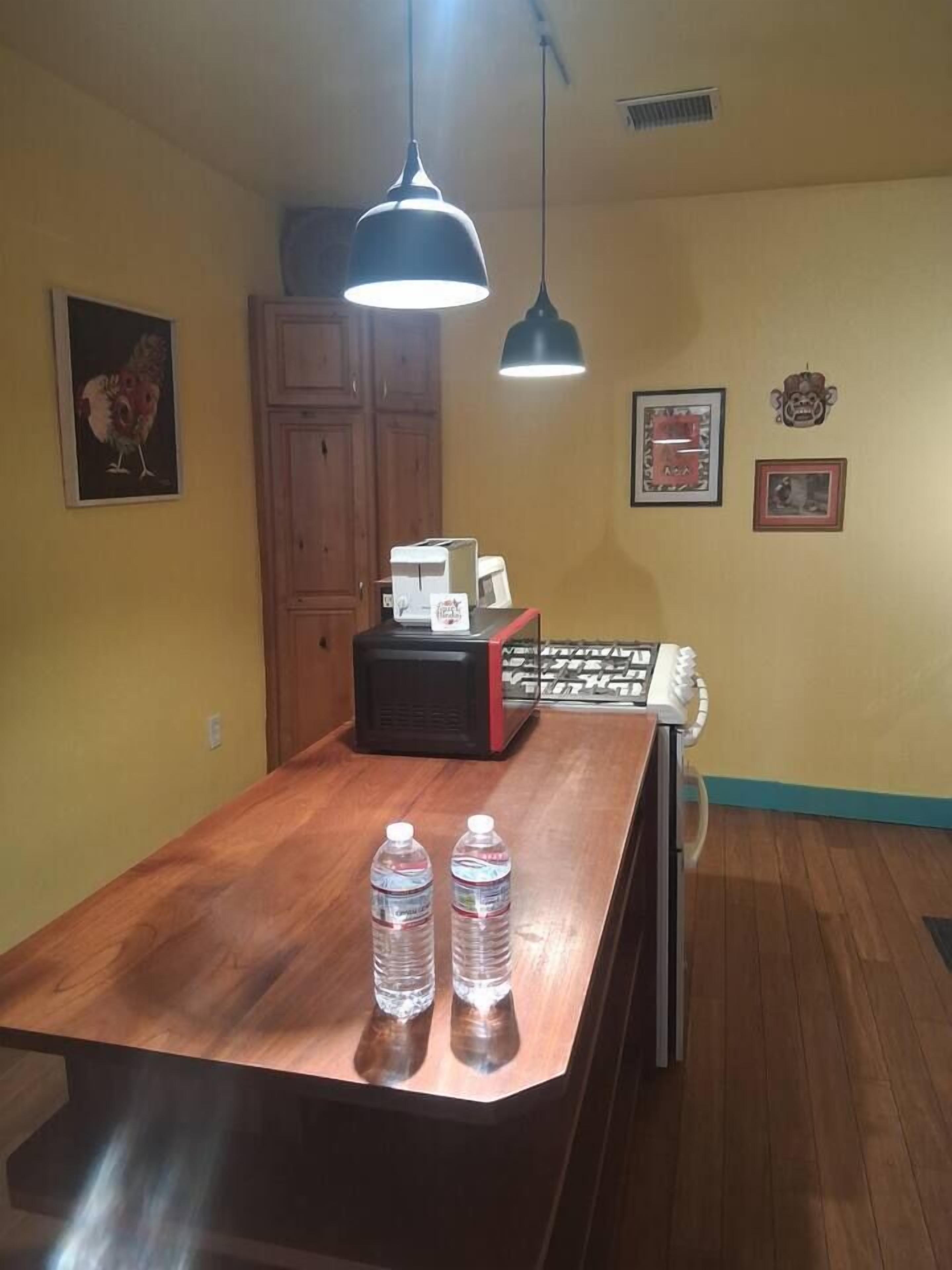 A room with a wooden table, two bottles, a microwave, and a cabinet.