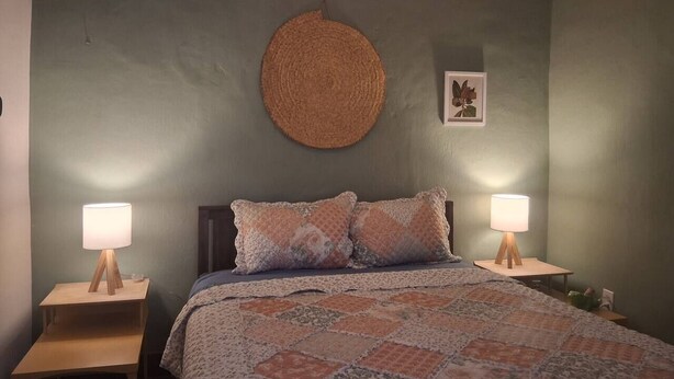 A bedroom with a bed, two bedside lamps, a circular wall hanging, and a framed picture. - Charming Historic Las Cruces House & Farmers Market (Las Cruces)