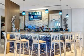 A modern bar area with a stone wall, multiple liquor bottles, and bar stools. - Portofino- Gulf Front with Beautiful Sunsets! (Escambia County)