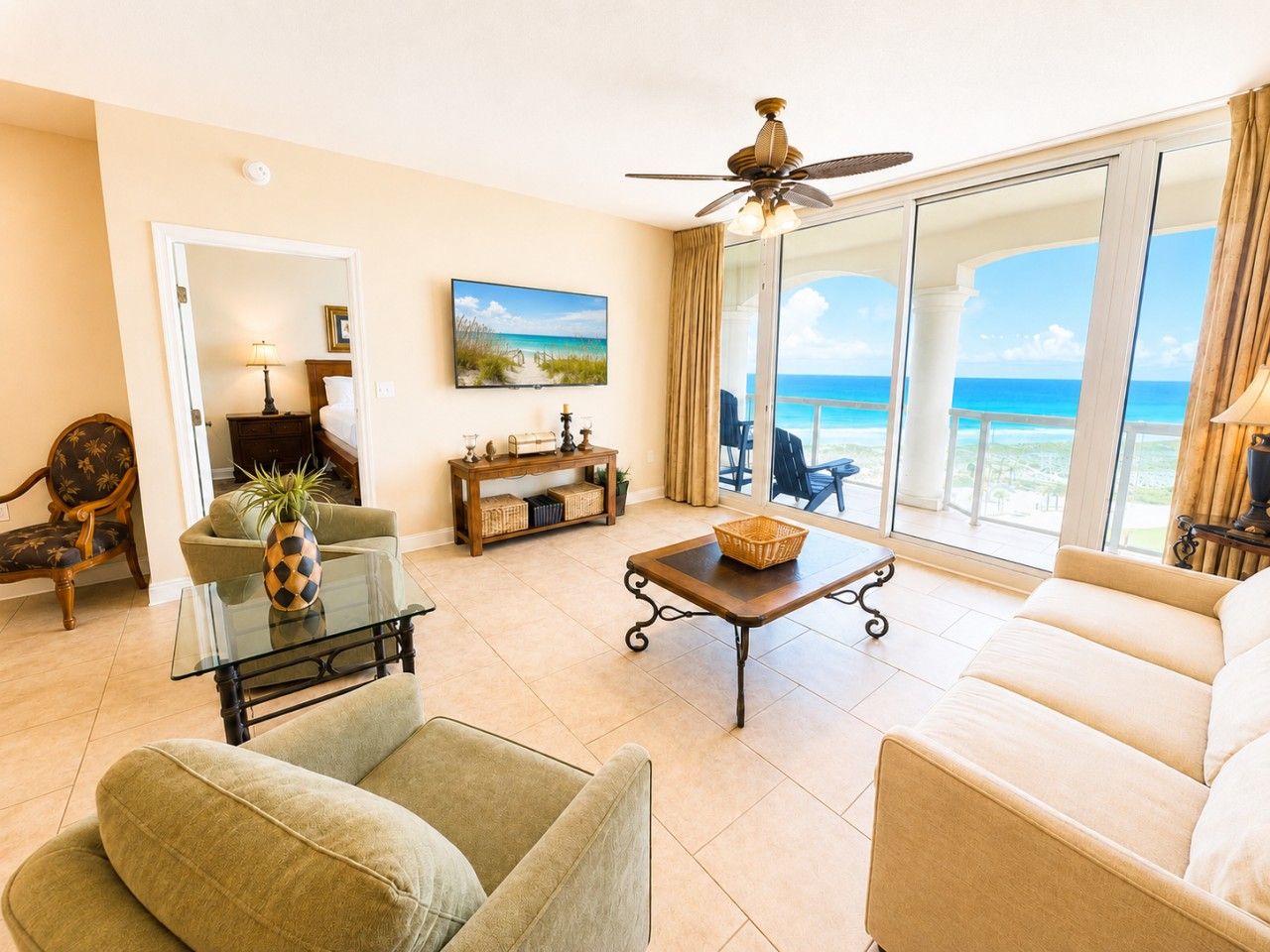 A living room with a sofa, armchairs, a coffee table, and a TV. There is a view of the ocean through large glass doors.