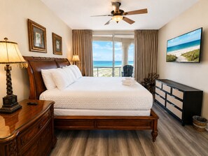 A hotel room with a bed, a desk, a dresser, a television, and a view of the beach. - Portofino- Gulf Front with Beautiful Sunsets! (Escambia County)