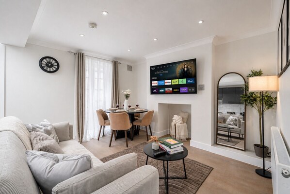 Una sala de estar moderna con sofá, mesa de comedor y sillas, un televisor de pantalla plana montado en la pared y un espejo grande.