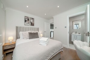 Un dormitorio moderno con cama, lámparas de noche, cabecera y vistas al baño.