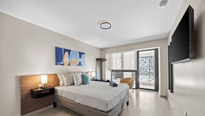 Quarto de hotel moderno com uma cama grande, televisão de tela plana, um quadro e vista da cidade pela janela.