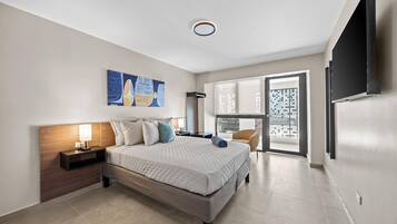 A modern hotel room with a large bed, a flat-screen TV, a painting, and a view of the city through the window.