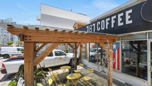 Café com mesas ao ar livre, pérgola de madeira e uma placa grande exibindo o número 181.