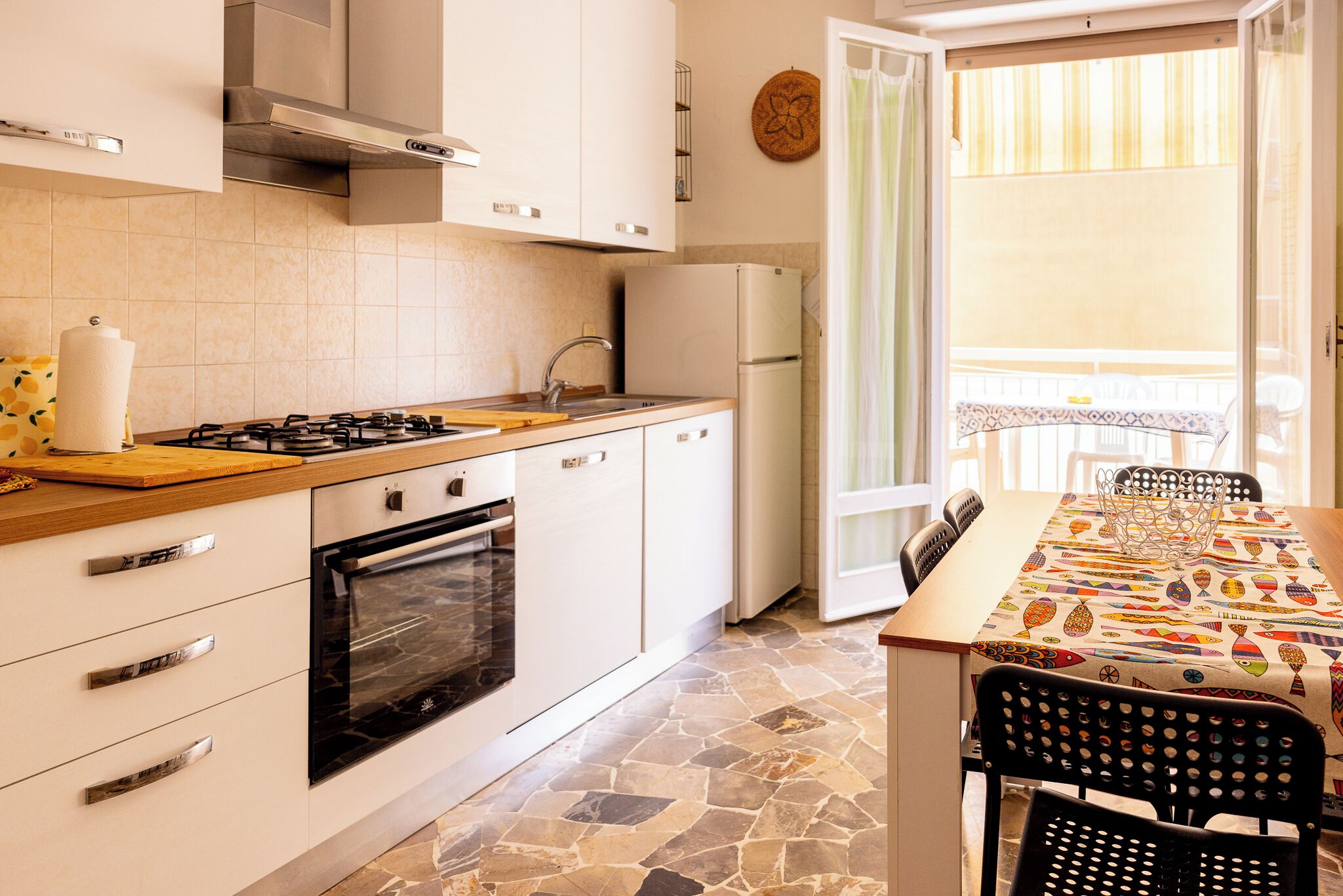 A compact kitchen with a gas stove, oven, and a refrigerator. There's a dining area with a table and chairs, and a balcony with a view.