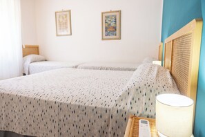 Ett hotellrum med två sängar, ett nattduksbord med en lampa och två inramade tavlor på väggen.