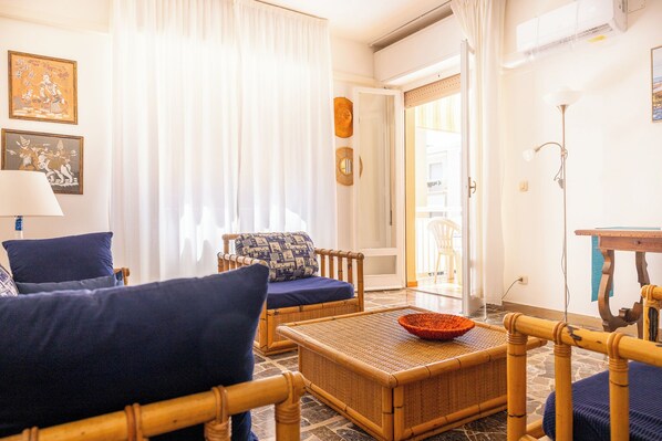 Una sala de estar con muebles de mimbre, un cojín estampado y un cuenco decorativo sobre una mesa tejida.