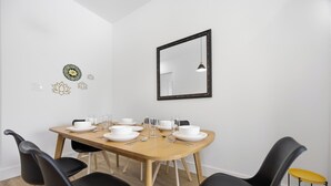 Uma sala de jantar com uma mesa de madeira posta para quatro pessoas, cadeiras pretas, um espelho com moldura preta e decorações nas paredes.