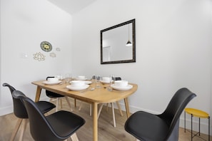 Zona pranzo con tavolo in legno apparecchiato per quattro persone, sedie nere, specchio con cornice nera e decorazioni alle pareti.