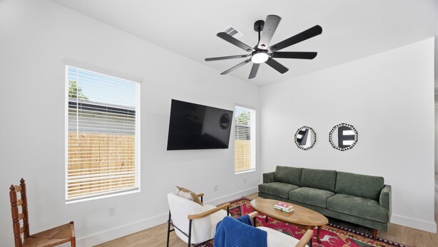 Sala de estar com sofá verde, cadeira de madeira, mesa de centro e ventilador de teto.