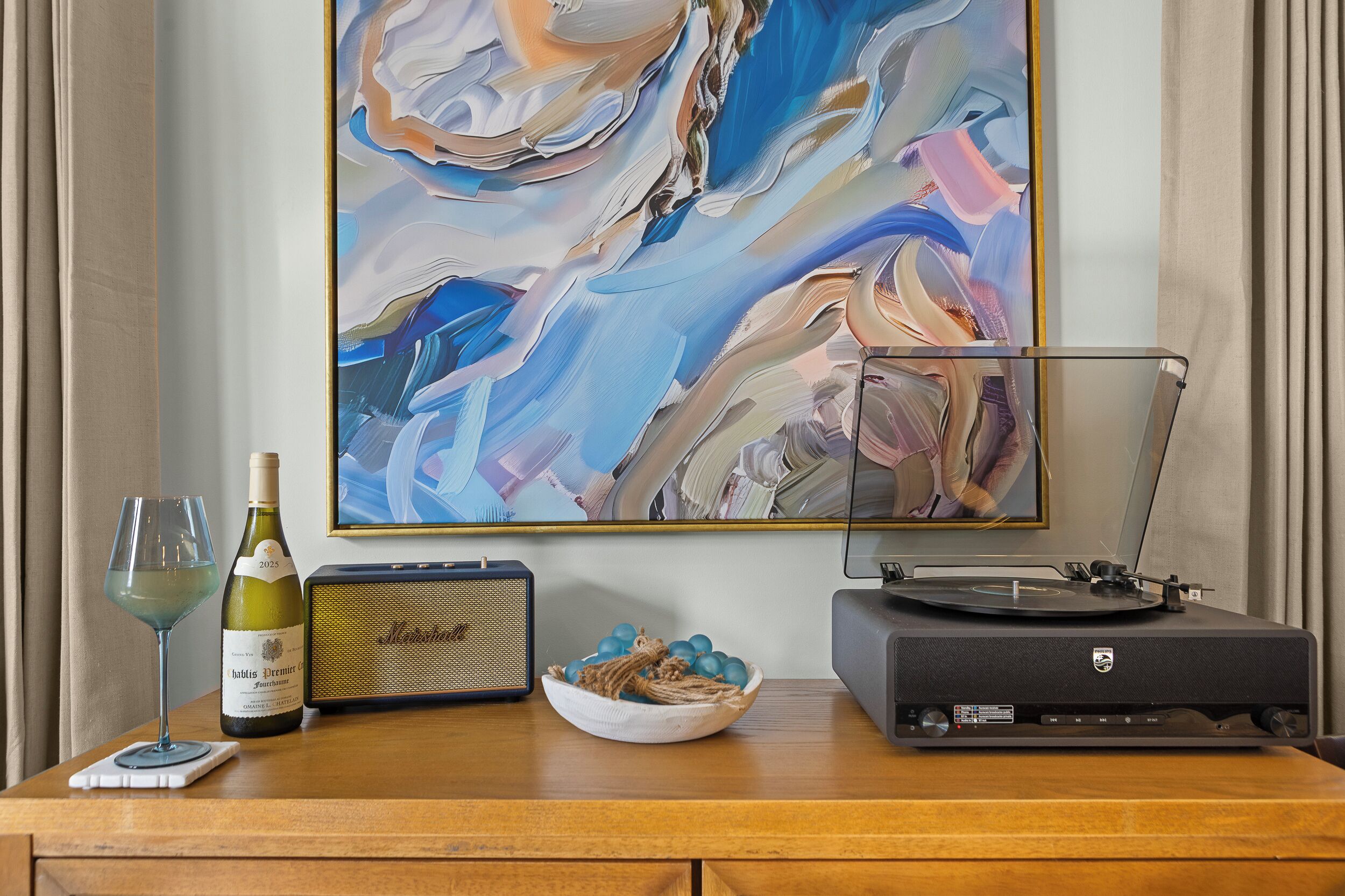Una mesa de madera con una botella de vino, una radio, un cuenco de adornos azules y un tocadiscos.
