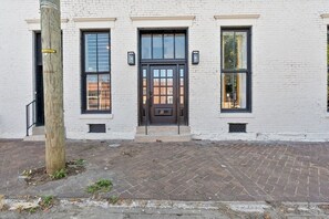 A white brick building with a black door, two windows on either side, and a brick-paved entrance. - Hot Tub | 6BR-4BA | Sleep 12+ | Game Rm | Fire Pit (Louisville)