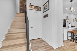 A staircase leading to a white door, a kitchen area with a bar stool, and a hanging light fixture. - Hot Tub | 6BR-4BA | Sleep 12+ | Game Rm | Fire Pit (Louisville)