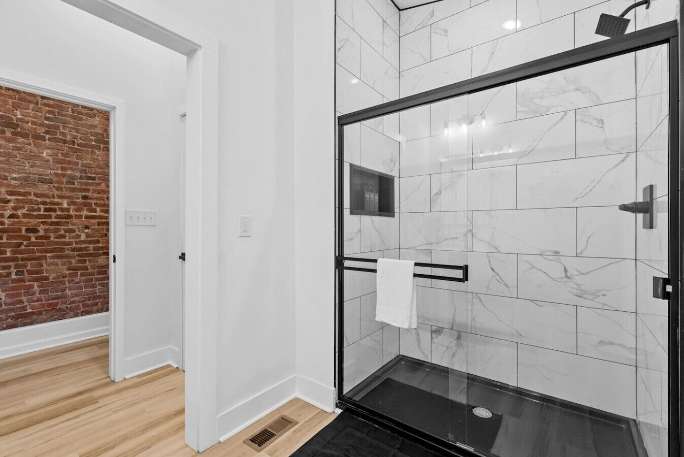 Un baño moderno con cabina de ducha de vidrio, azulejos de mármol y suelo de madera.