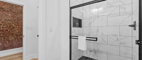Un baño moderno con cabina de ducha de vidrio, azulejos de mármol y suelo de madera.