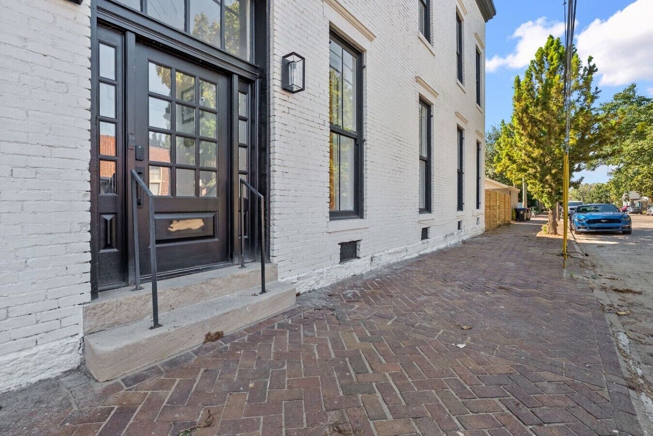 A building with a white brick facade, large windows, and a paved walkway.