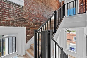 A staircase with black railings leading to a room with white trim and a brick wall. - Hot Tub | 6BR-4BA | Sleep 12+ | Game Rm | Fire Pit (Louisville)