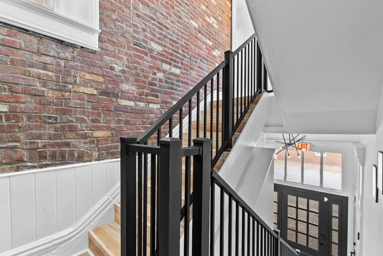 A staircase with black railings leading to a landing with a white door and a window with an exit sign.