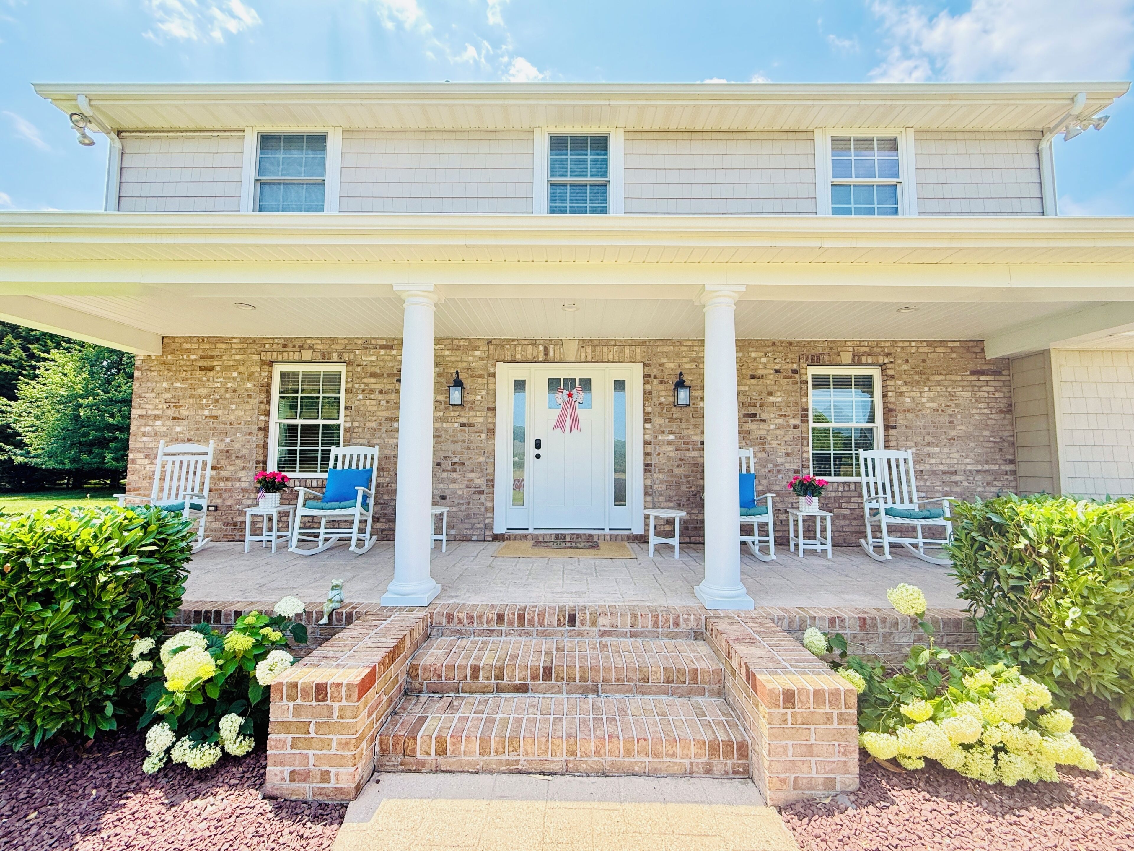A two-story house with a covered porch, brick exterior, and white columns.