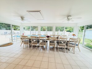 A sunlit room with a dining table and chairs, large windows, and ceiling fans. - Spacious 6-bedroom house with a pool, gameroom, office & plenty of free parking (Rehoboth Beach)