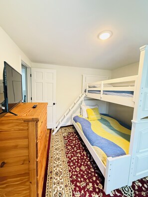 Une chambre avec des lits superposés, un bureau en bois, une télévision et un tapis à motifs.