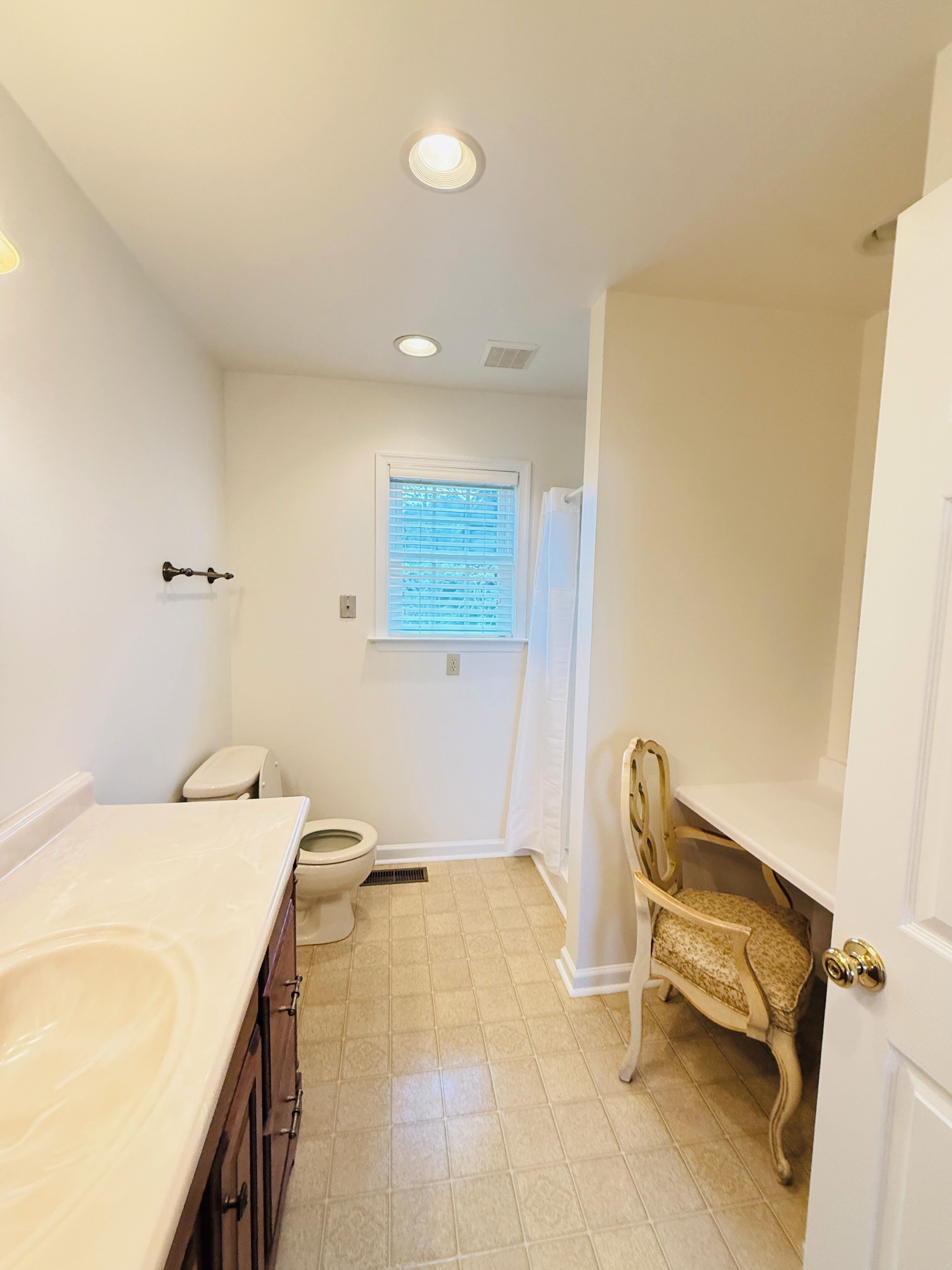 Een badkamer met toilet, wastafel, opbergmeubel en een stoel.