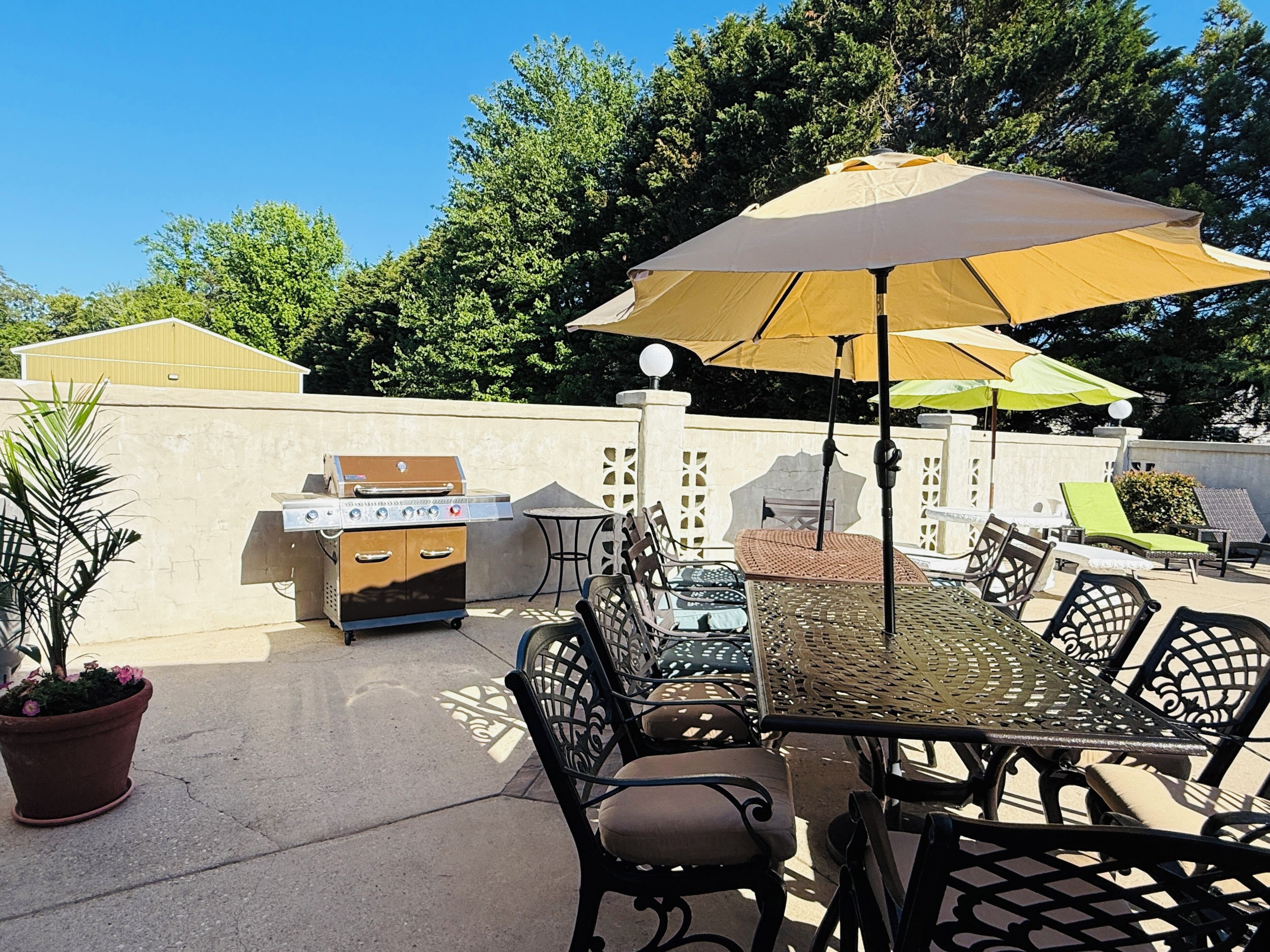 An outdoor patio with a grill, dining table, chairs, and umbrellas.