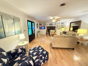 A living room with a sofa, ottoman, and chairs, a fireplace, television, and a ceiling fan. - Spacious 6-bedroom house with a pool, gameroom, office & plenty of free parking (Rehoboth Beach)