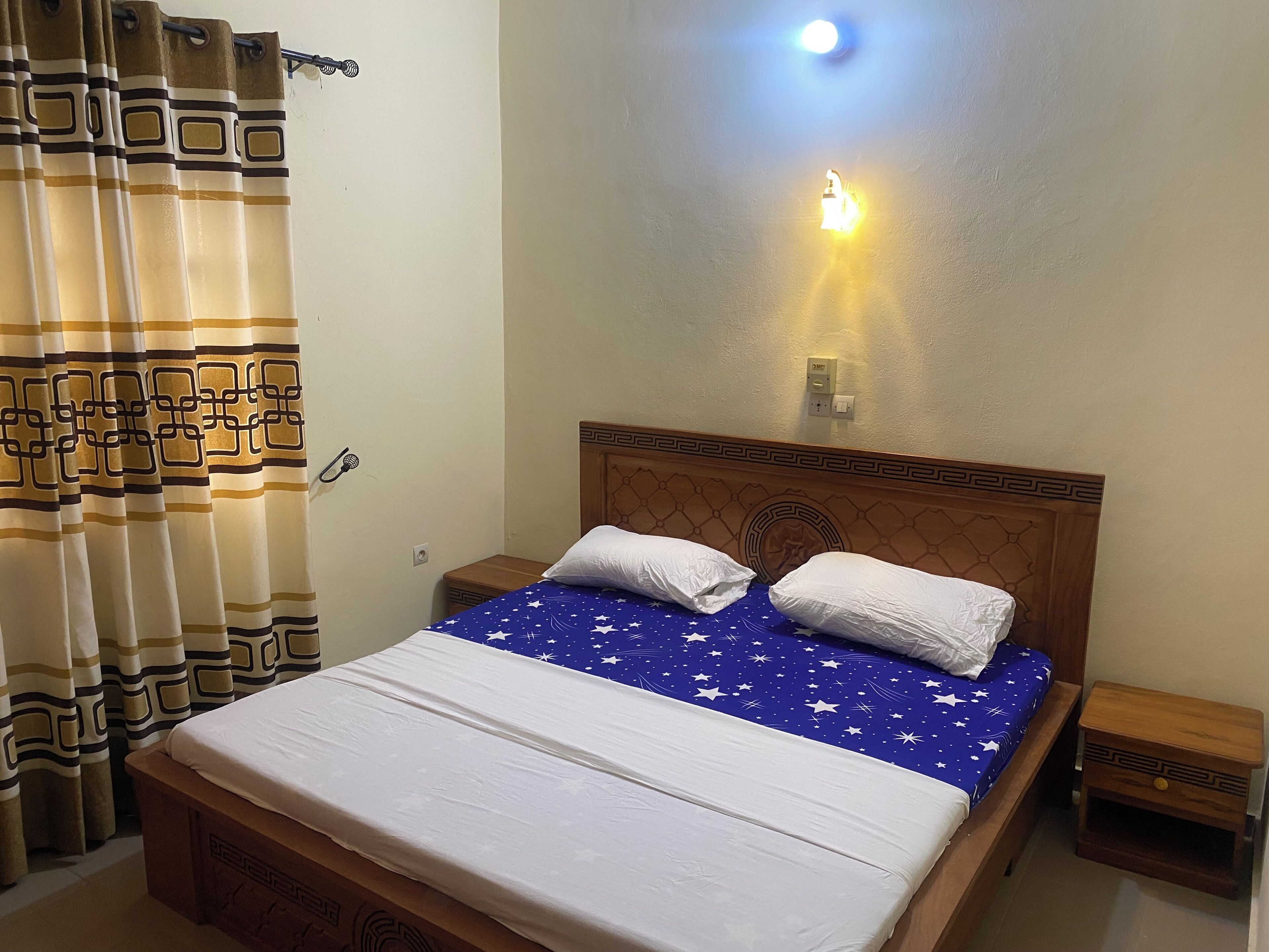 A neatly made bed with a blue star-patterned bedspread, a wooden headboard, and two bedside tables with lamps.