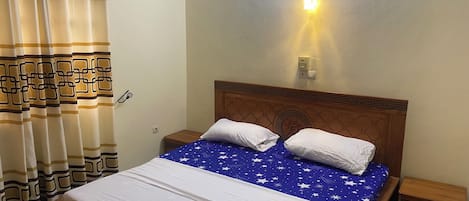 A neatly made bed with a blue star-patterned bedspread, a wooden headboard, and two bedside tables with lamps.