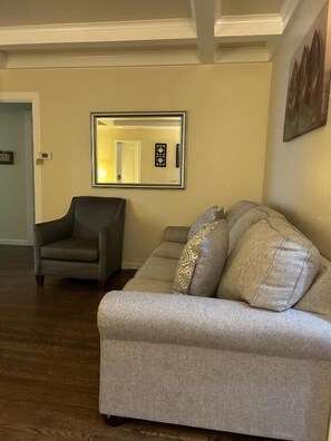 Een woonkamer met een grijze bank, een grijze fauteuil en een spiegel aan de muur.