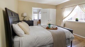 A bedroom with a bed, bedside table, lamp, and a window with curtains. - Spacious Room Prime Silicon valley (Palo Alto)