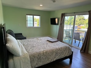 Een slaapkamer met een bed, televisie, raam en balkon.