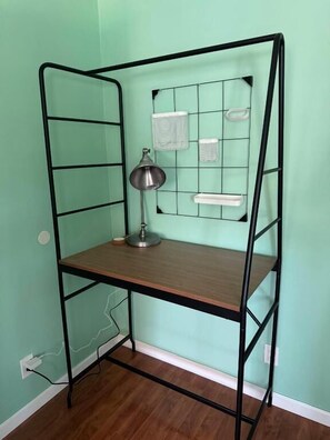 Una cama litera de metal con escritorio y estanterías frente a una pared verde.