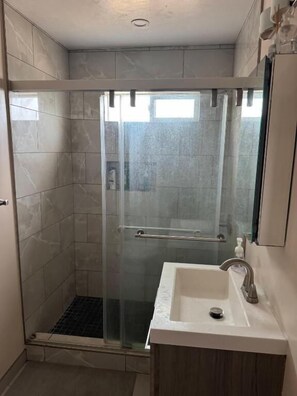 A bathroom with a glass-enclosed shower, a sink, and a mirror.